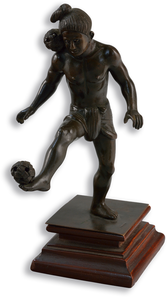 Bronze statue of a man wearing only a loincloth who is balancing a ball on his right foot and another on his right shoulder.